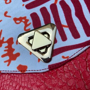 May include: A close-up of a gold-toned triangular clasp on a red and white patterned fabric bag.