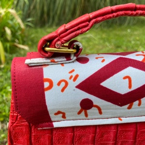 May include: A red handbag with a gold clasp and a white fabric lining with a geometric pattern. The handbag has a red leather strap.