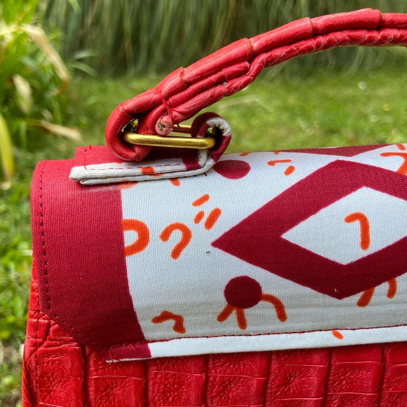 May include: A red handbag with a gold clasp and a white fabric lining with a geometric pattern. The handbag has a red leather strap.