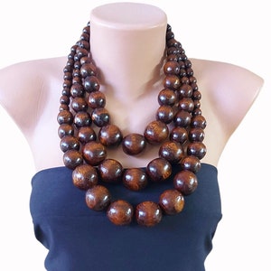 May include: A multi-strand necklace made of large, dark brown wooden beads. The necklace is layered and has a chunky, statement look.