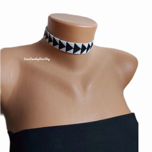 May include: A black and white beaded choker necklace with a geometric pattern. The necklace is made of small, round beads that are strung together to create a triangular design.