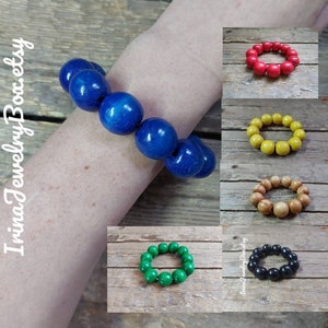 May include: A set of wooden bead bracelets in various colors, including blue, red, yellow, brown, green, and black. The bracelets are made of round wooden beads and are shown on a wooden surface.