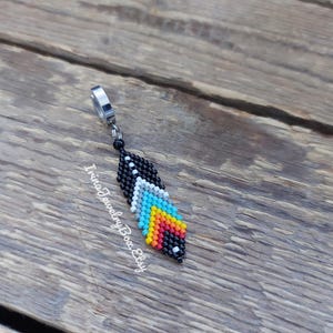 May include: A beaded feather earring with a black, white, blue, yellow and orange colour scheme. The earring is attached to a silver-toned metal hook.
