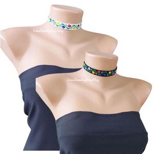 May include: Two beaded chokers on mannequins. One is white with colourful floral patterns, the other black with similar designs. The mannequins wear black strapless tops. The text "IrinaJewelryBoxEtsy" is visible.