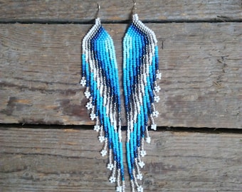 May include: A pair of long, beaded earrings with a gradient of blue and white beads. The earrings are made with small, round beads and have a fringe-like design.