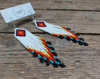 May include: A pair of white beaded earrings with a diamond-shaped design. The earrings feature a fringe of white beads with accents of orange, yellow, turquoise, and black beads.