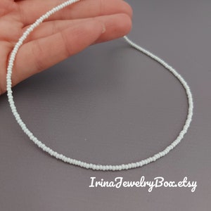 May include: A delicate white beaded necklace with a silver clasp. The necklace is approximately 16 inches long and is made with tiny seed beads.
