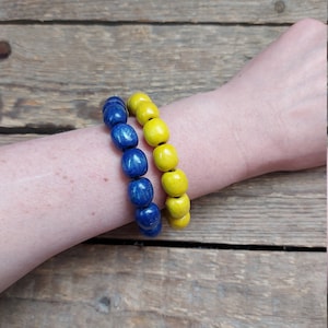 Può includere: Due braccialetti fatti di perline di legno. Un braccialetto è blu e l'altro è giallo.