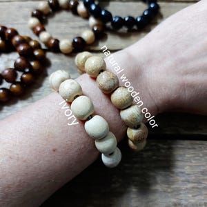 May include: Wooden bead bracelets in various colors, including ivory, natural wood, and black. The bracelets are displayed on a wooden surface, with the text "natural wooden color" and "ivory" visible.