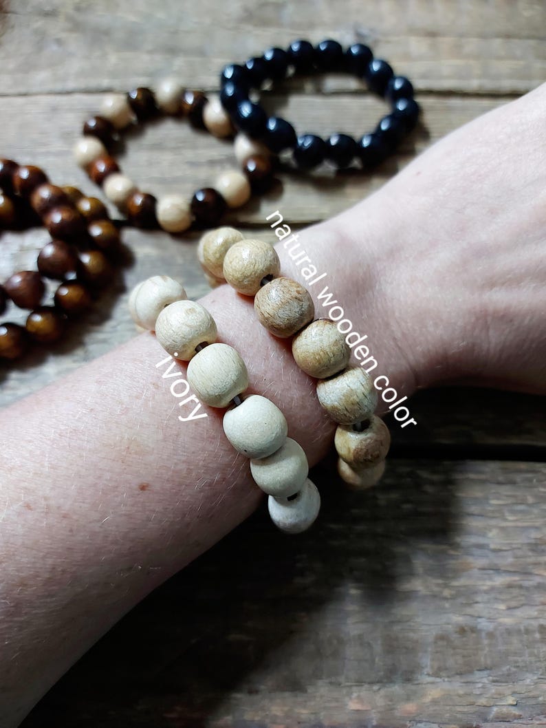 May include: Wooden bead bracelets in various colors, including ivory, natural wood, and black. The bracelets are displayed on a wooden surface, with the text "natural wooden color" and "ivory" visible.