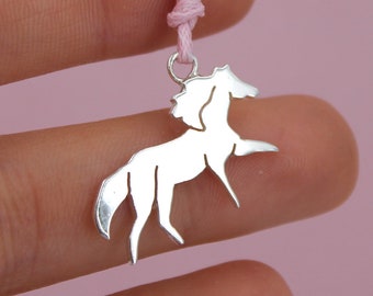 May include: A silver horse pendant necklace on a pink cord. The horse is a simple silhouette with a flowing mane.