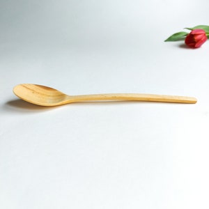 May include: A wooden spoon with a natural finish. The spoon is curved and has a long handle.