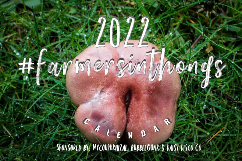 Puede incluir: Un calendario de 2022 con el hashtag #farmersinthongs. El calendario presenta un primer plano de una seta rosada y carnosa con una profunda hendidura en el centro. La seta est&aacute; sentada sobre un lecho de hierba verde con gotas de roc&iacute;o.