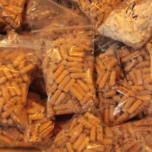 May include: Multiple clear plastic bags filled with small, brown, wooden pellets. The bags are stacked on top of each other.