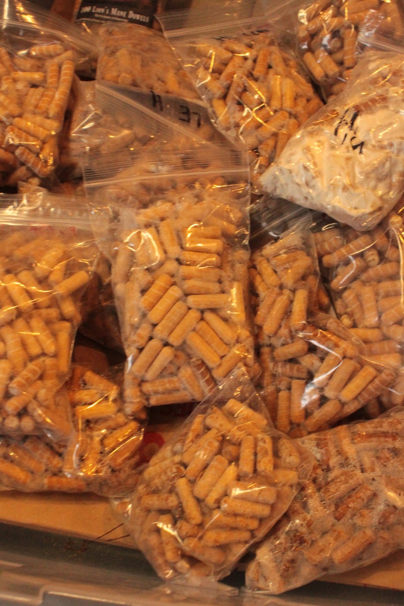 May include: Multiple clear plastic bags filled with small, brown, wooden pellets. The bags are stacked on top of each other.