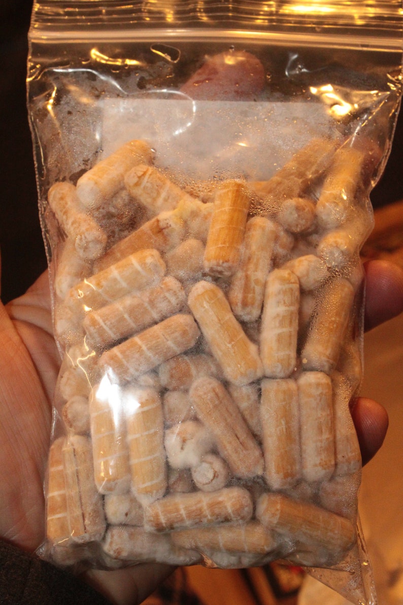 May include: A clear plastic bag filled with a large quantity of small, wooden dowels. The dowels are all the same size and are arranged in a random pattern. The dowels are a light brown color and have a smooth, polished finish.