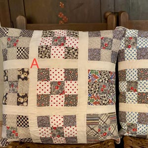 May include: Two square throw pillows with patchwork designs. Pillow A features squares of red, black, and floral patterns. Pillow B has blue and brown squares. Both pillows have a cream-colored grid pattern.