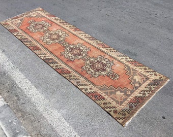 May include: A vintage runner rug with a traditional Persian design. The rug has a red, orange, and beige color scheme with intricate patterns.