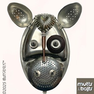 May include: A whimsical metal sculpture of a dog's face, crafted from repurposed kitchen utensils. The ears are slotted spoons, the eyes are a dark brown circle and a metal button, and the nose is a perforated ladle. The sculpture has a unique, industrial aesthetic.