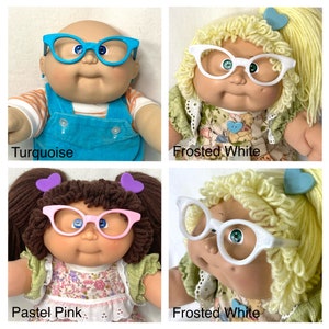 May include: Four Cabbage Patch Kids dolls wearing different coloured glasses. The glasses are turquoise, frosted white, and pastel pink. The text "Turquoise", "Frosted White", and "Pastel Pink" are below the dolls.