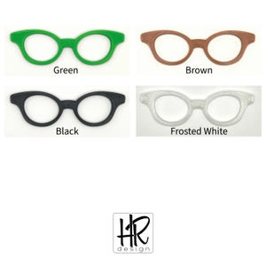 May include: Four pairs of spectacles in various colours: green, brown, black, and frosted white. Each pair has a classic, rounded frame design. The image includes the text "Green", "Brown", "Black", and "Frosted White" below each pair.