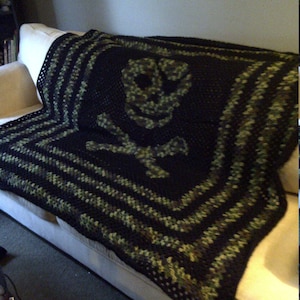 May include: A black and green crocheted throw blanket with a skull design. The blanket is on a white couch.