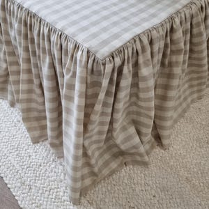 May include: A beige and white checkered table with a ruffled skirt. The table is covered with a fabric featuring a classic gingham pattern. The skirt adds a decorative element to the table's design.