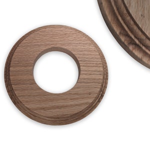 May include: A wooden ring with a circular hole in the center. The ring has a natural wood finish and a slightly raised edge.