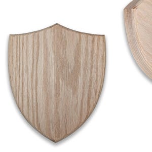 May include: Two unfinished wooden shield plaques with a natural wood grain pattern. The shields are light brown and have a classic crest shape, perfect for crafting or display.