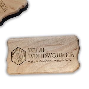 May include: A light-colored wooden tool with rounded edges, featuring the text "WILD WOODWORKER" and the phrase "Make it Wooden. Make it Wild." A hexagonal graphic is also present. The tool appears to be a woodworking accessory.