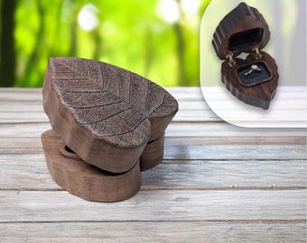 May include: A wooden ring box shaped like a leaf, with a detailed leaf vein pattern carved into the top. The box is open in the inset image, revealing a ring inside. The box is brown and sits on a wooden surface.