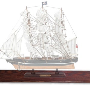 May include: A wooden model ship with white sails and a black hull. The ship is on a wooden base with a nameplate that reads "Cutty Sark".