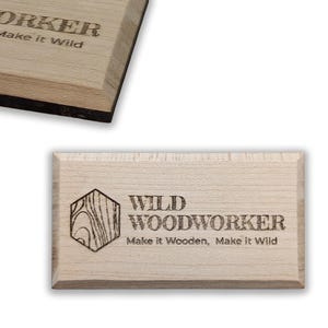 May include: Light-colored wooden sign with the text "WILD WOODWORKER" and "Make it Wooden, Make it Wild" in a dark font. The sign features a geometric design. The wood has a natural grain.