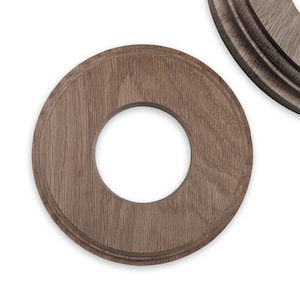 May include: Two wooden, circular decorative elements with a central hole. The wood has a natural grain and a warm brown tone. One element is in focus, while a partial view of another is visible in the background.