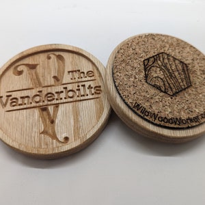 May include: Two wooden coasters, one with a cork top and the other with a carved wooden top. The cork coaster has a hexagonal design and the text "WillowWoodWorker.com". The wooden coaster has the text "The Vanderbilts" and a carved letter "V".