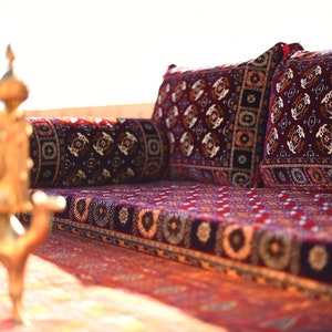 Puede incluir: Un sofá tradicional de Oriente Medio con cojines estampados en rojo, negro y blanco y una alfombra a juego. El sofá está hecho de madera y tiene un perfil bajo.