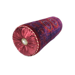May include: A red and blue patterned cylindrical cushion with a burgundy satin end cap and a gold button in the centre. The cushion is decorated with a traditional Persian design.