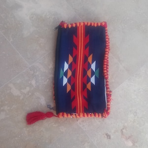 May include: A blue and red woven zippered pouch with a tassel. The pouch has a geometric pattern with orange, white, and green accents.