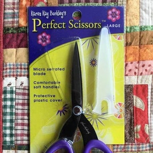 May include: Purple-handled scissors with black blades, packaged on a yellow and blue card. The package reads "Karen Kay Buckley's Perfect Scissors" and lists features like a micro-serrated blade and comfortable handles. A protective plastic cover is included.