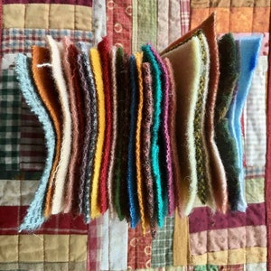 May include: A stack of colorful felt squares in various shades of brown, orange, yellow, red, green, blue, and teal. The felt squares are arranged in a vertical stack, with the edges of each square visible.