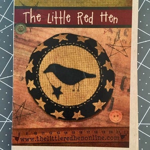 May include: A brown card with the text "The Little Red Hen" in red and white lettering. The card features a black crow with a star in its beak, surrounded by a circle of gold stars on a black background. The card also includes a red button and a ruler with the text "www.thelittleredhenonline.com".