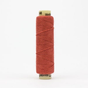 May include: A spool of terracotta colored thread with the text "Woolcraft" on the label.