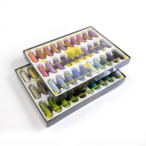 May include: Two stacked boxes of colorful embroidery thread spools. The spools are arranged in rows within a clear plastic container. The thread colors include shades of pink, purple, blue, green, and yellow. The boxes have the word "Wonders" printed on them.