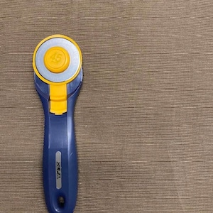 May include: A blue and yellow rotary cutter with a 45 mm blade. The cutter is on a brown textured surface.