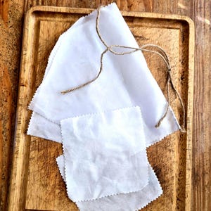 May include: White fabric squares and a triangle are arranged on a wooden tray, tied with twine. The fabric has a textured, slightly wrinkled appearance. The wooden tray and background are a warm, natural wood tone.
