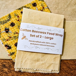 May include: Two large cotton beeswax food wraps. One wrap is yellow with a pattern of bees, pinecones, and leaves. The other wrap is a solid beige color. A label reads "Cotton Beeswax Food Wrap Set of 2 - Large."