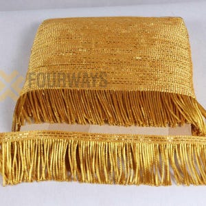 Op de afbeelding: Gouden franjeband met een geweven textuur. De band heeft een dik, rechthoekig stuk en een dunnere strook, beide met lange, vloeiende franjes. De band is helder, metallic goud van kleur.