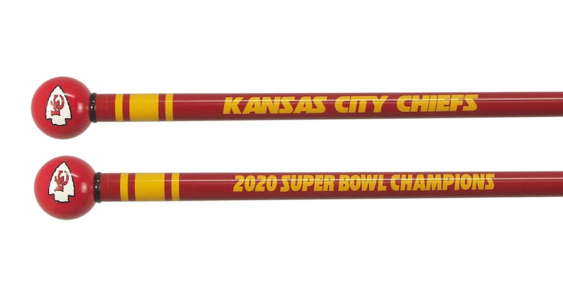 May include: Two red and yellow wooden drumsticks with a Kansas City Chiefs logo on the top. The top drumstick says "Kansas City Chiefs" and the bottom drumstick says "2020 Super Bowl Champions".