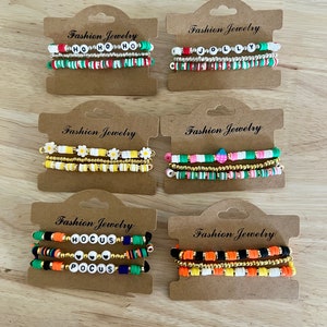May include: Set of six colorful beaded bracelets with different letter combinations, including "HO HO HO", "JOLLY", "HOCUS POCUS", and a floral design. The bracelets are displayed on brown card stock with the words "Fashion Jewelry" printed on each card.
