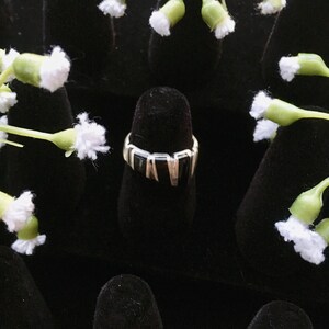 May include: A black and silver ring with a geometric design. The ring is on a black velvet display stand.